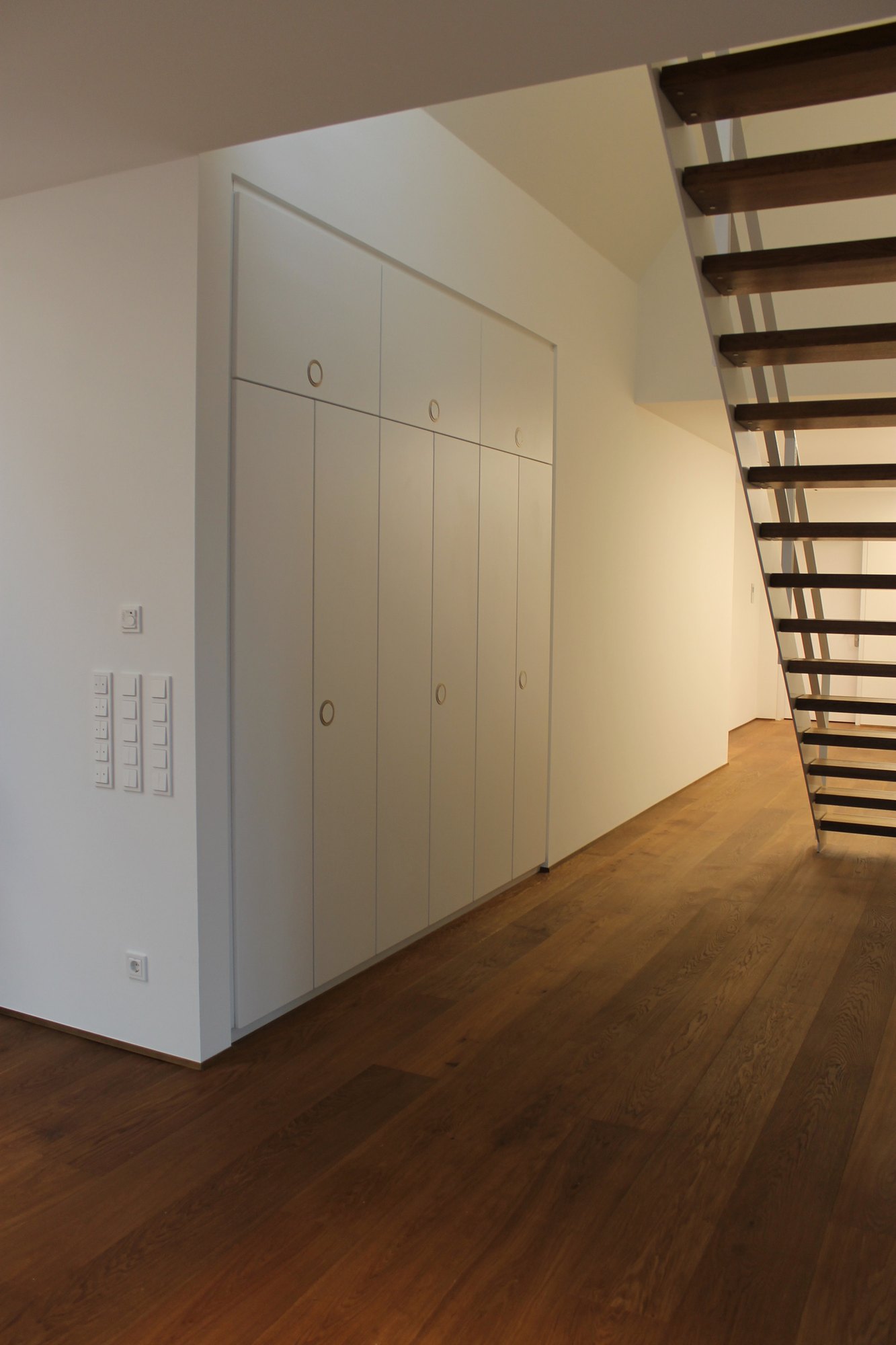 Raumhoher weißer Einbauschrank in einem Flur, rechts eine Treppe mit offenen Stufen