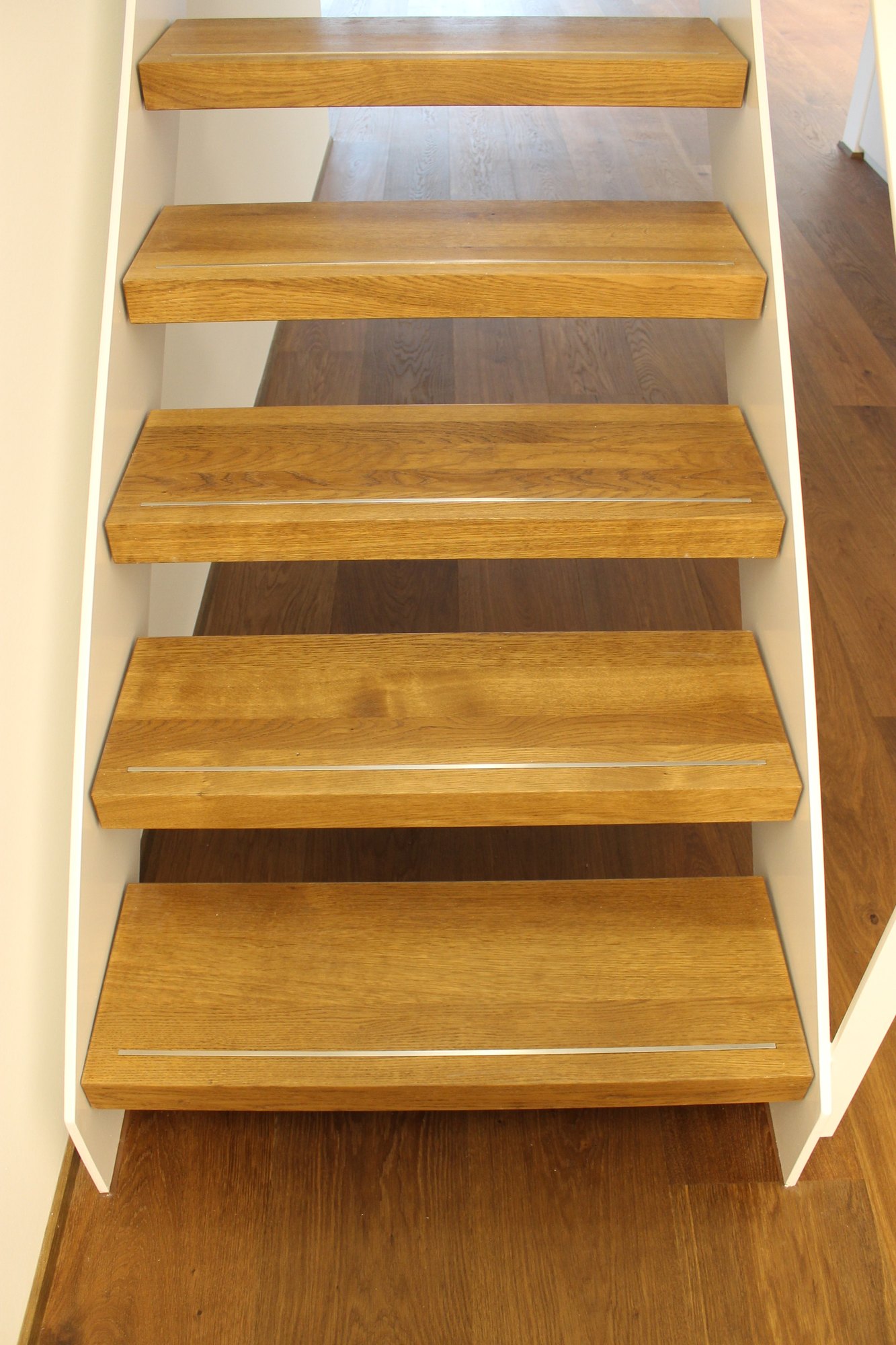 Treppe mit offenen Stufen aus Holz, aufgenommen von oben, daneben ein weißes Wangenblech