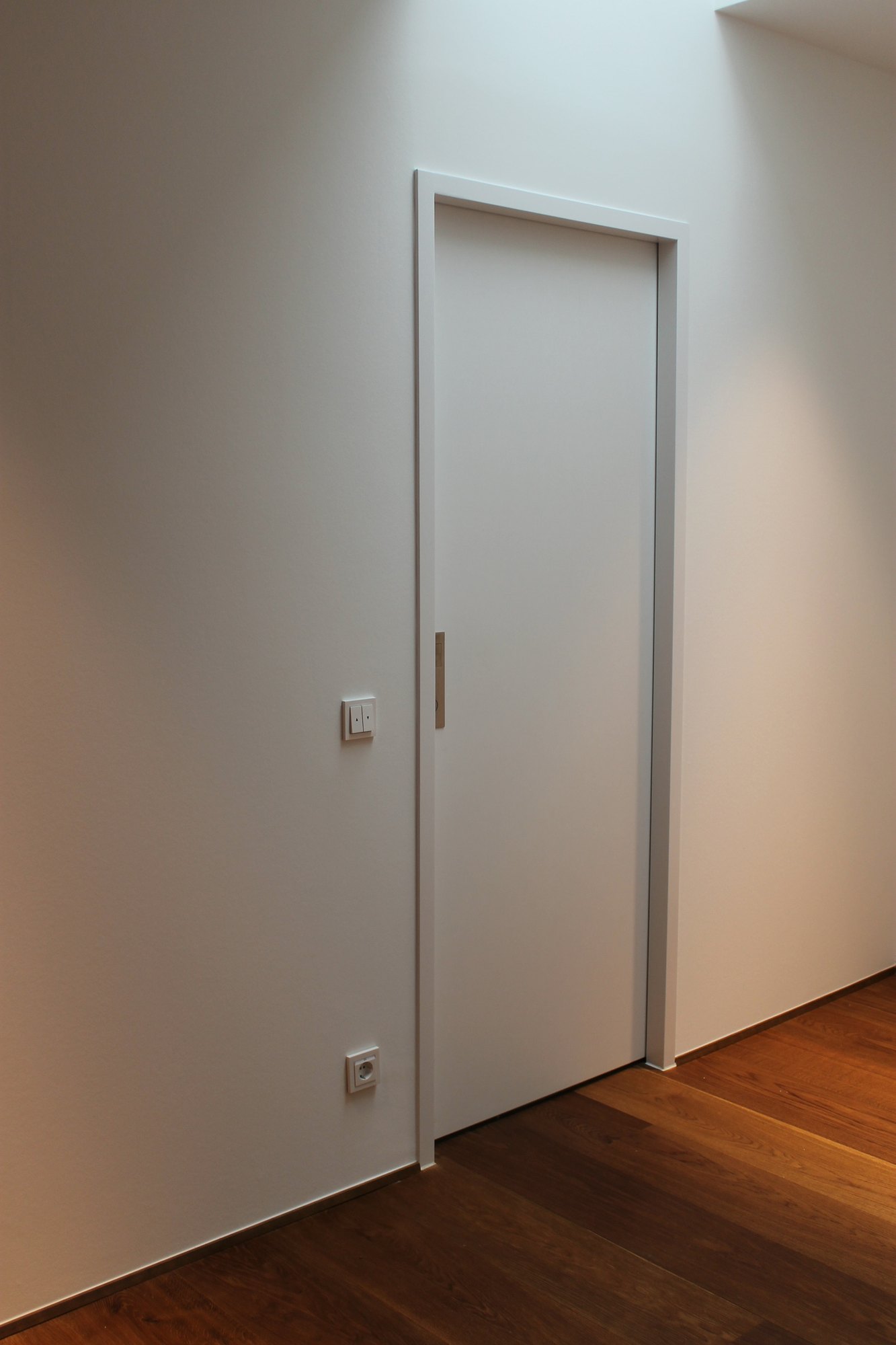 Weiße Tür, flächenbündig in die Wand eingebaut, mit schmalem senkrechtem Griff